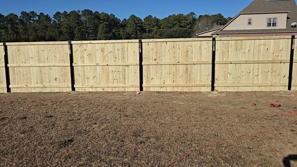 A new wood privacy fence with black posts installed in a backyard by Fayetteville Fence Pros in Fayetteville, NC.