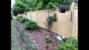 A newly installed wood privacy fence with decorative post caps and landscaping by Premier Fence of Birmingham, LLC in Warrior, AL.