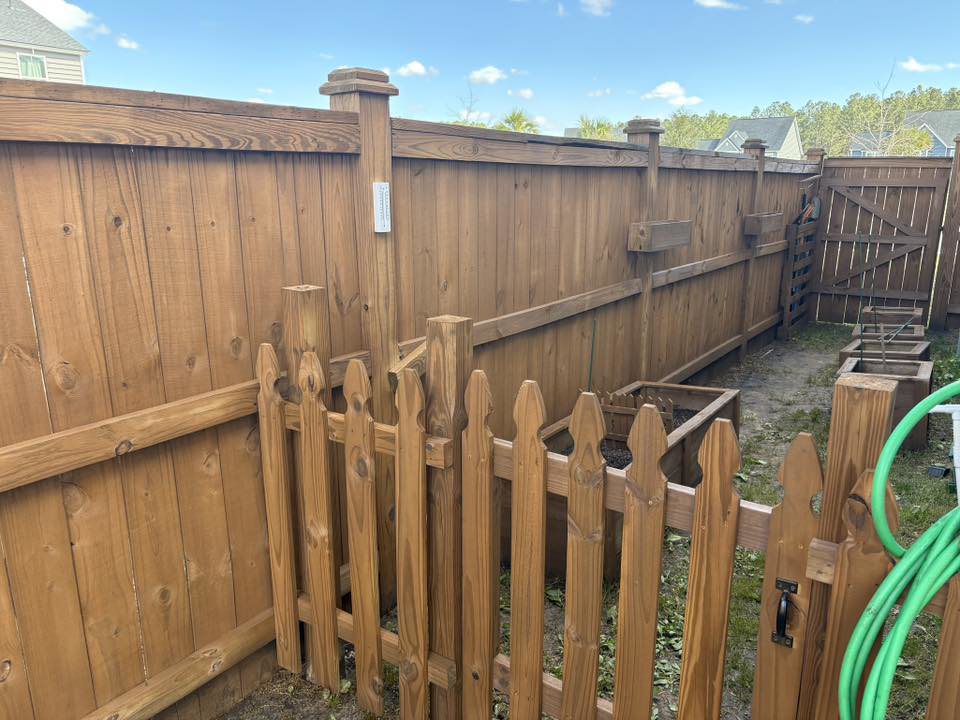 A stained wood privacy fence featuring a small picket gate leading to a garden area, installed by Stain and Go in Summerville, SC.