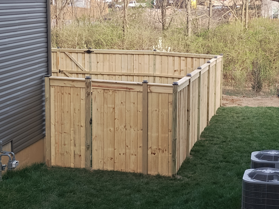 A new wood privacy fence with a gate installed around AC units by Veteran Fence in North Royalton, OH.