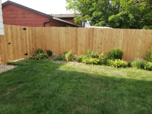 A wood privacy fence with a gate, bordering a landscaped backyard, installed by JBC Services LLC in Milwaukee, WI.