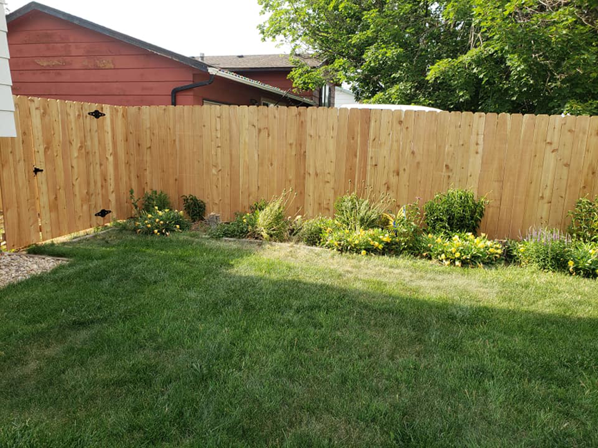 A wood privacy fence with a gate, bordering a landscaped backyard, installed by JBC Services LLC in Milwaukee, WI.