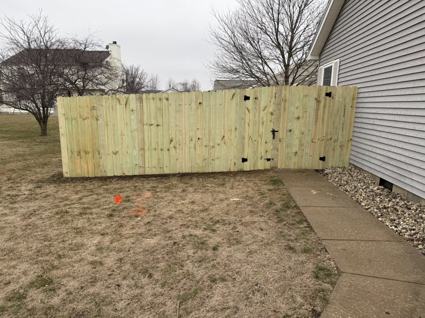A newly installed wood privacy fence with a gate next to a residential home by Heath's Outdoor Services LLC in Champaign, IL.