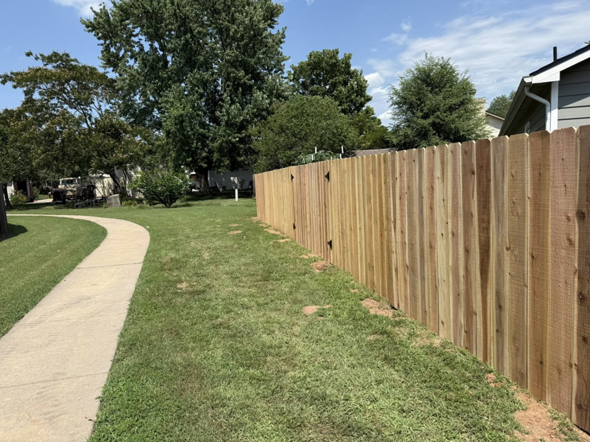 A newly installed wood privacy fence with a gate next to a sidewalk by NC Fencing LLC in Wichita, KS.