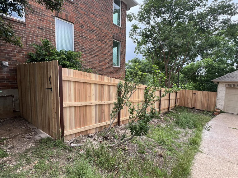 A new wood privacy fence with a gate installed alongside a brick residential home by K.K. Landscaping & Fencing in Austin, TX.