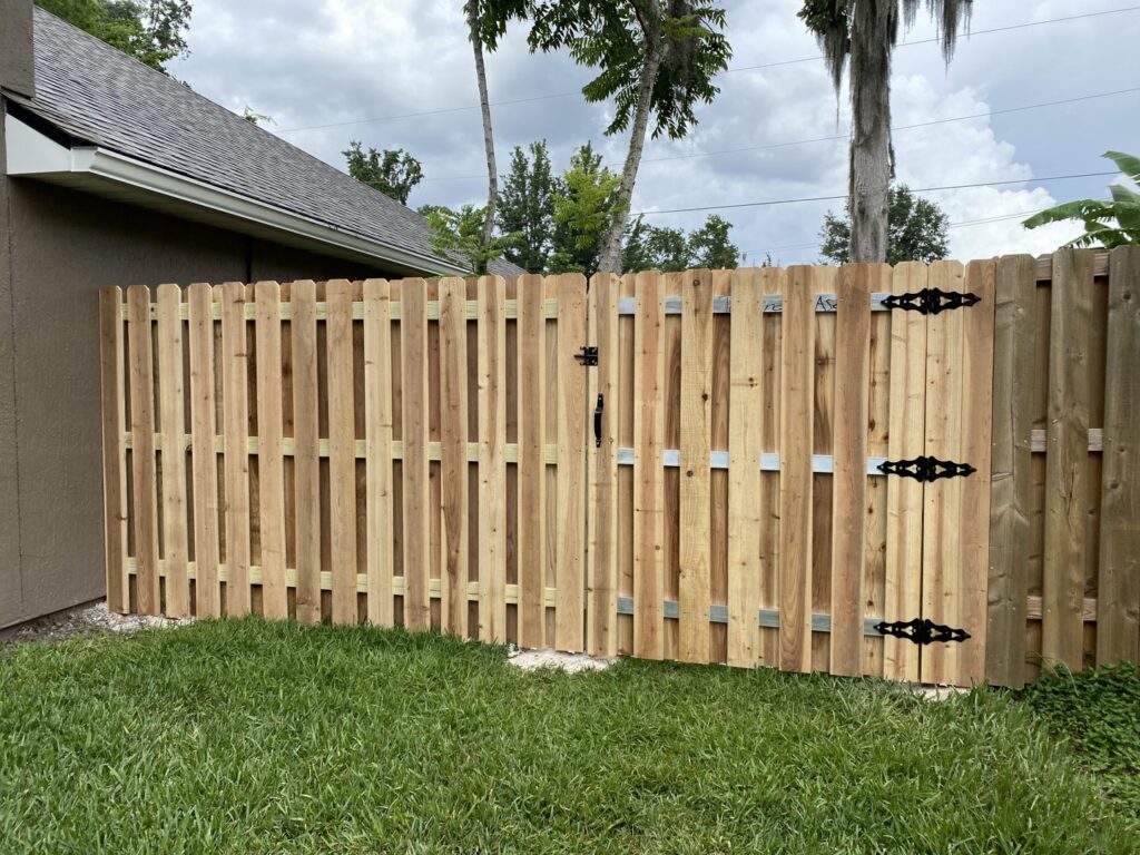 A newly installed wood privacy fence with a gate and decorative hinges by Top Fence LLC in Jacksonville, FL.
