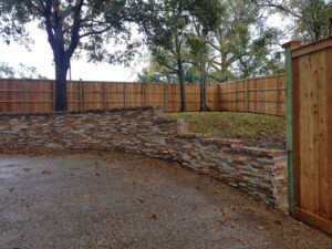 A long wood privacy fence installed behind a decorative stone retaining wall by A-1 Security Fence in Scott, LA.