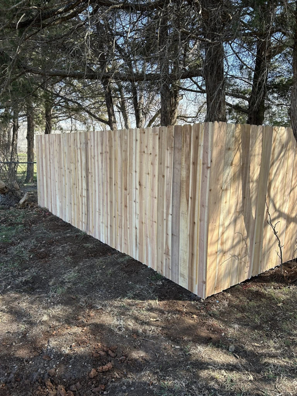 A newly installed wood privacy fence in a wooded area by NC Fencing LLC in Wichita, KS.