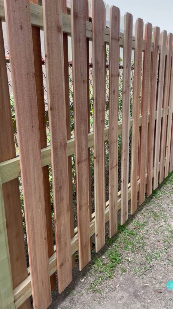 Wood privacy slats being installed onto an existing chain-link fence by 985 Fence, LLC in Schriever, LA.