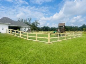 A wooden split-rail fence with wire mesh enclosing a spacious backyard with a playset, installed by Capitol Fencing in Baton Rouge, LA.