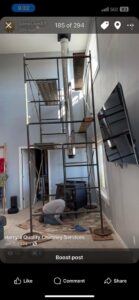 A worker installing a wood stove and chimney pipe indoors with scaffolding, performed by Harry's Quality Chimney Services in Kansas City, MO