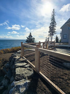 A wood and wire mesh fence installed along a scenic coastline by Midcoast Fence in Northport, ME.