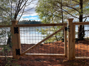 A wood and wire mesh fence with a gate overlooking a body of water by Midcoast Fence in Northport, ME.