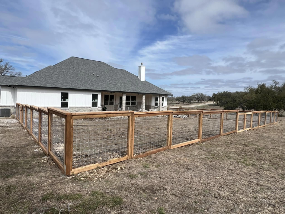A newly installed wood and wire mesh perimeter fence surrounding a large property by K.K. Landscaping & Fencing in Austin, TX.