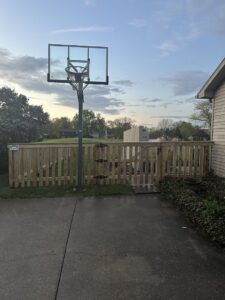 A wooden backyard fence with an integrated gate, installed near a basketball hoop by NBBJ Fence LLC in Bluffton, IN.