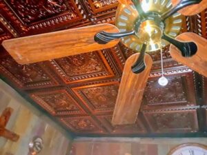 A wooden blade ceiling fan installed against a decorative tin ceiling by Calvert Electrical Service in San Antonio, TX