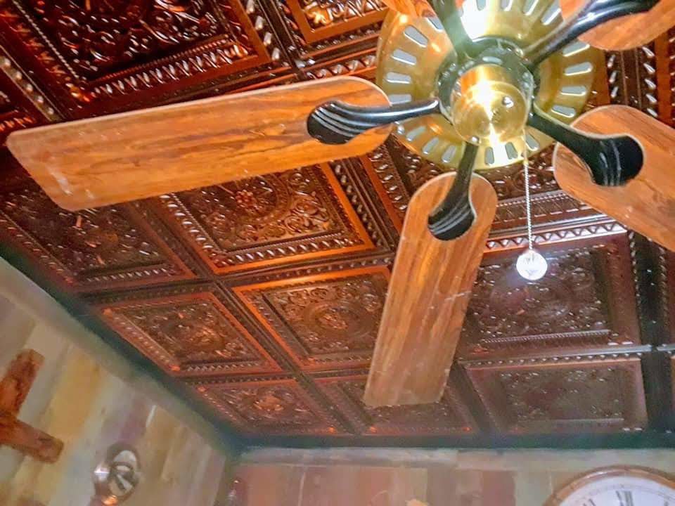 A wooden blade ceiling fan installed against a decorative tin ceiling by Calvert Electrical Service in San Antonio, TX