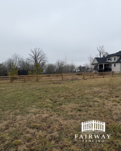A long wooden farm-style fence installed across a grassy field with a residential property in the background by Fairway Fencing in Lexington, KY.