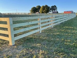 A long wooden farm-style fence with wire mesh installed in a rural setting by RUCO Fence in Huntsville, AL.