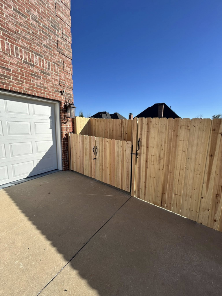 A sturdy wooden fence and gate installed alongside a residential garage by Timber Wolf Fence Co. in Rogers, AR.