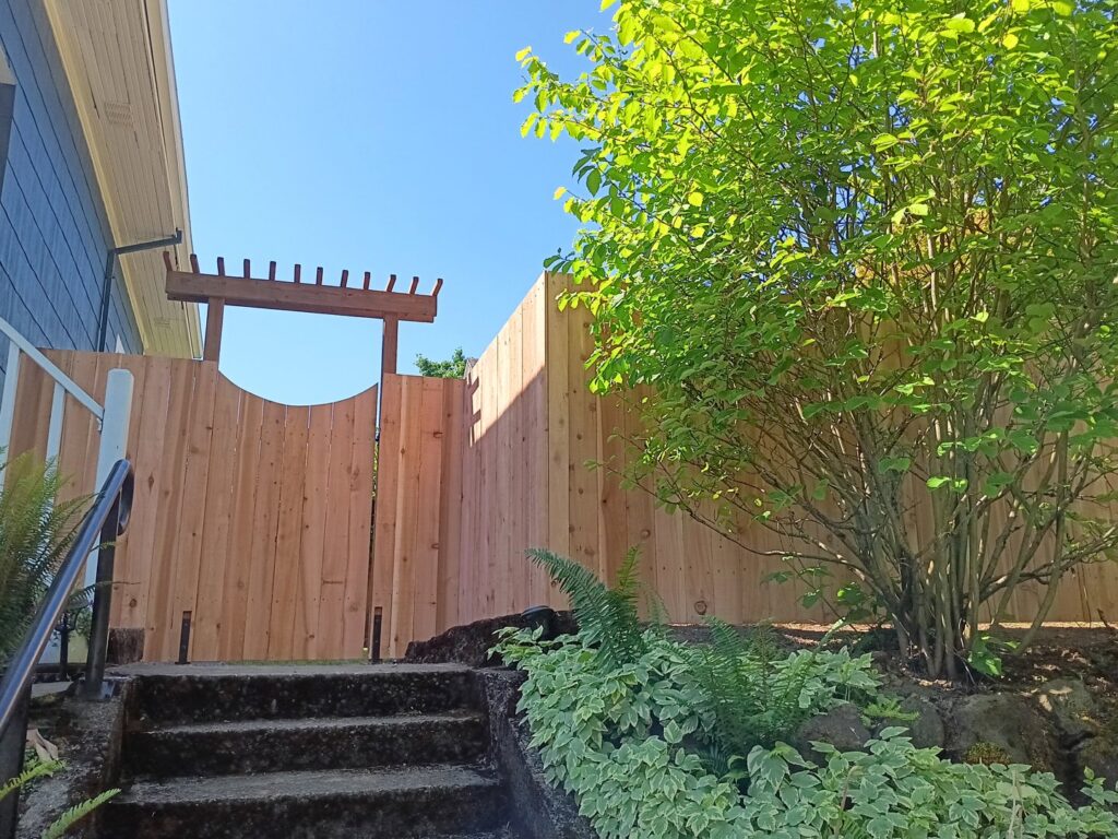 A wooden privacy fence with a gate and decorative arbor, seen from a side view, by Fix-A-Fence LLC in Portland, OR.