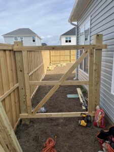 A wooden fence gate under construction with tools and materials on the ground by Heavenly Gates Construction LLC in Miami, FL