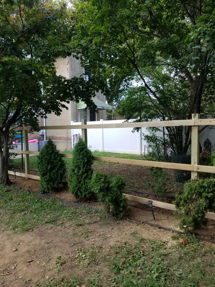 A wooden fence being installed in a backyard with small evergreen shrubs by Concord Fence Llc in Wilmington, DE