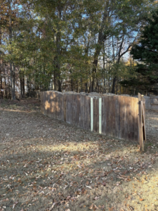 A wooden fence showing new panel replacements and a detached section, indicating repair work by Myers & Dunlap Fence Repair in Greenville, SC.