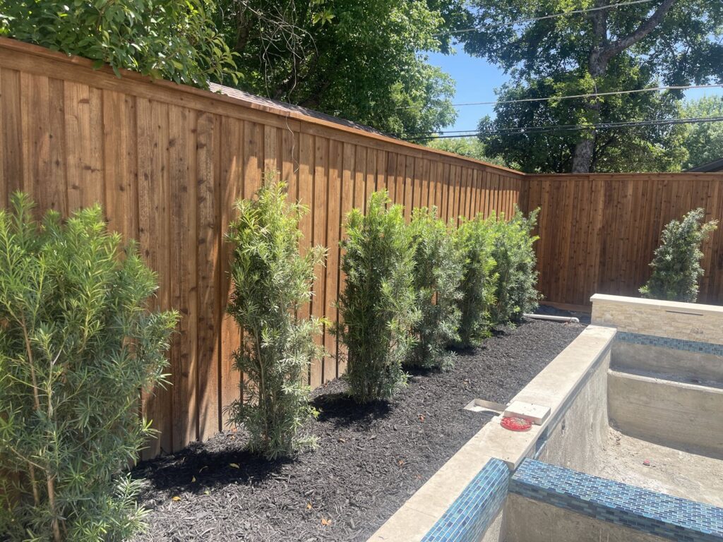 A newly installed wooden fence alongside a pool area with fresh landscaping by Backyard Builders in Rockford, MI.