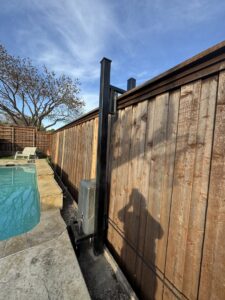 A wooden fence next to a swimming pool, featuring a gate post and operator by HDR Systems Gate, Fence & Garage doors in Plano, TX