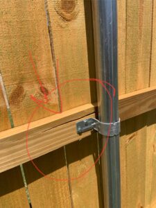 A close-up of a wooden fence post with a pipe attachment, showcasing detail work by Backyard Builders in Rockford, MI.