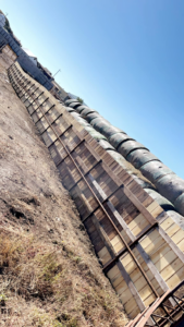 A robust wooden fence structure, possibly a windbreak or corral, next to large hay bales by Bighorn Fencing in Williston, ND.