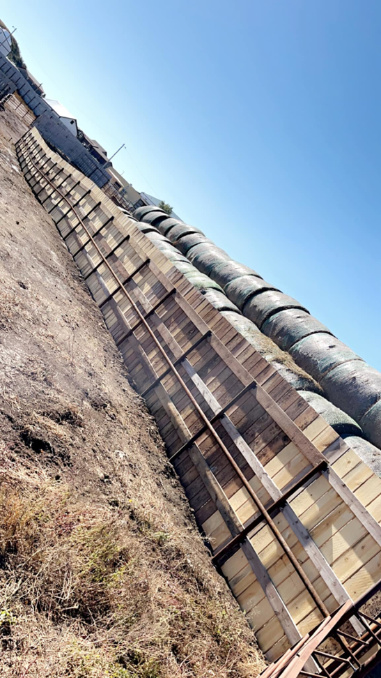 A robust wooden fence structure, possibly a windbreak or corral, next to large hay bales by Bighorn Fencing in Williston, ND.