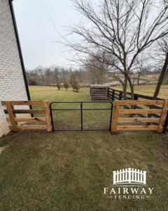 A wooden fence section with a black metal gate, installed next to a brick house by Fairway Fencing in Lexington, KY.