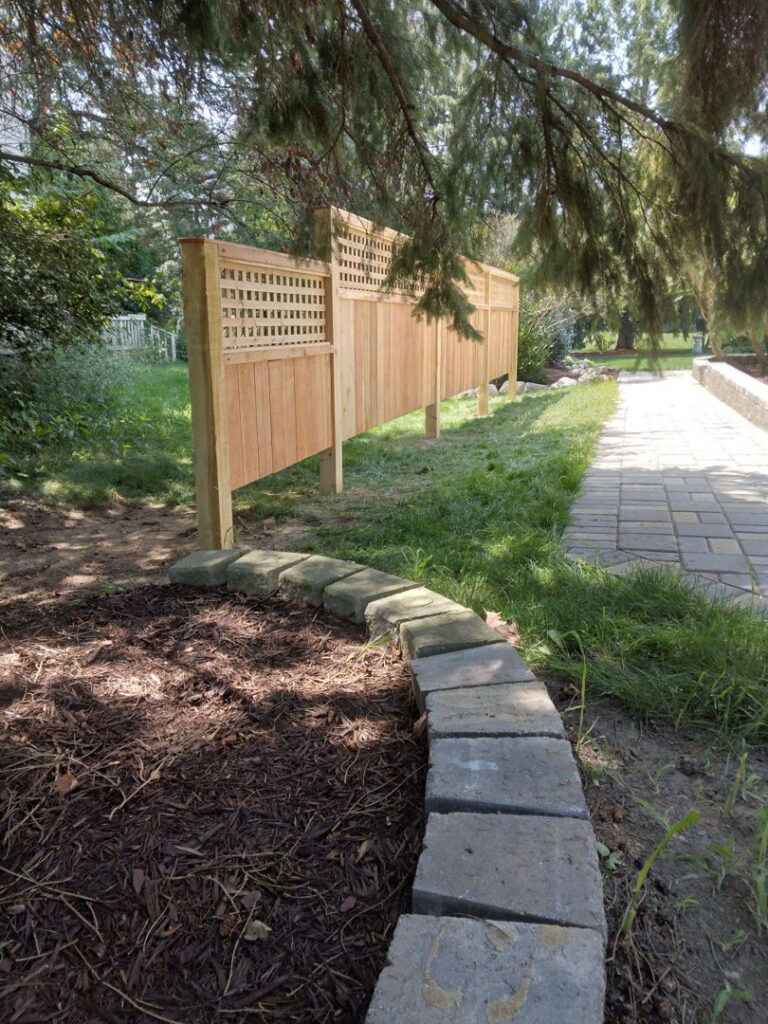 A wooden fence with a decorative lattice top installed along a pathway, showcasing work by Sparta Fencing in Ely, UK.