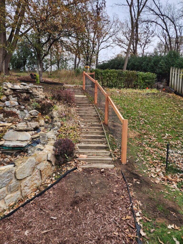 A wooden fence with wire mesh installed along a set of outdoor stairs on a sloped property by MN Mike's Fence and Repair in Lakeville, MN.