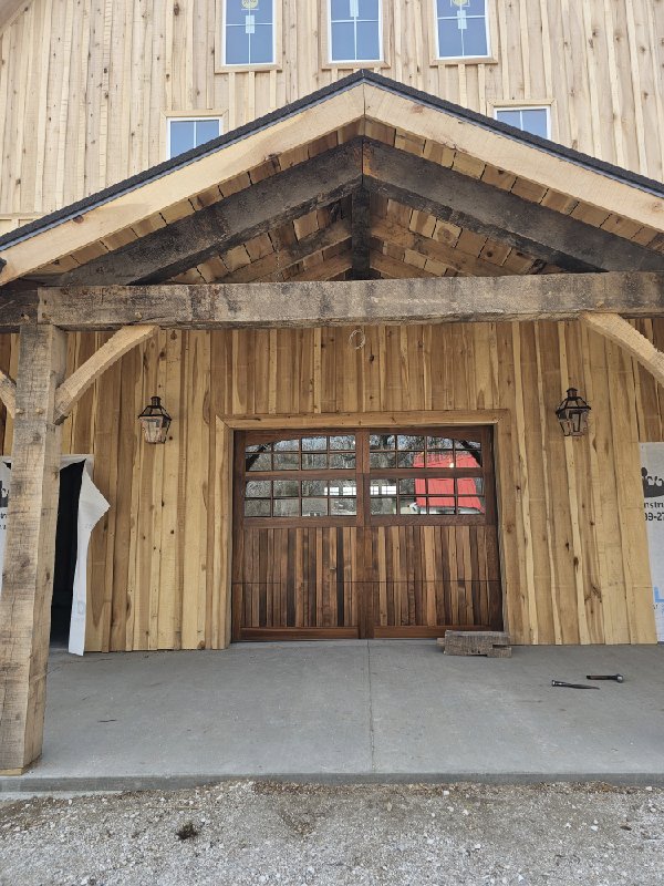 A beautiful wooden garage door with multiple windows installed on a rustic wooden building by Steve's Overhead Door Company in Lafayette, IN.