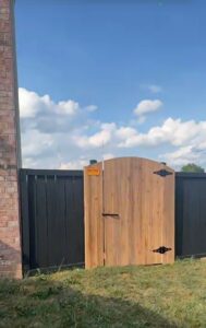 A custom wooden gate with decorative black hardware, integrated into a modern black privacy fence by Roark Fencing in Lexington, KY.