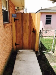 A new wooden gate installed next to a brick wall and an existing chain-link fence by Amko Fence Co. in Kenner, LA.