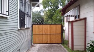 A custom wooden gate with a metal frame installed between two residential houses by Serrato's Fence & Welding in San Antonio, TX.