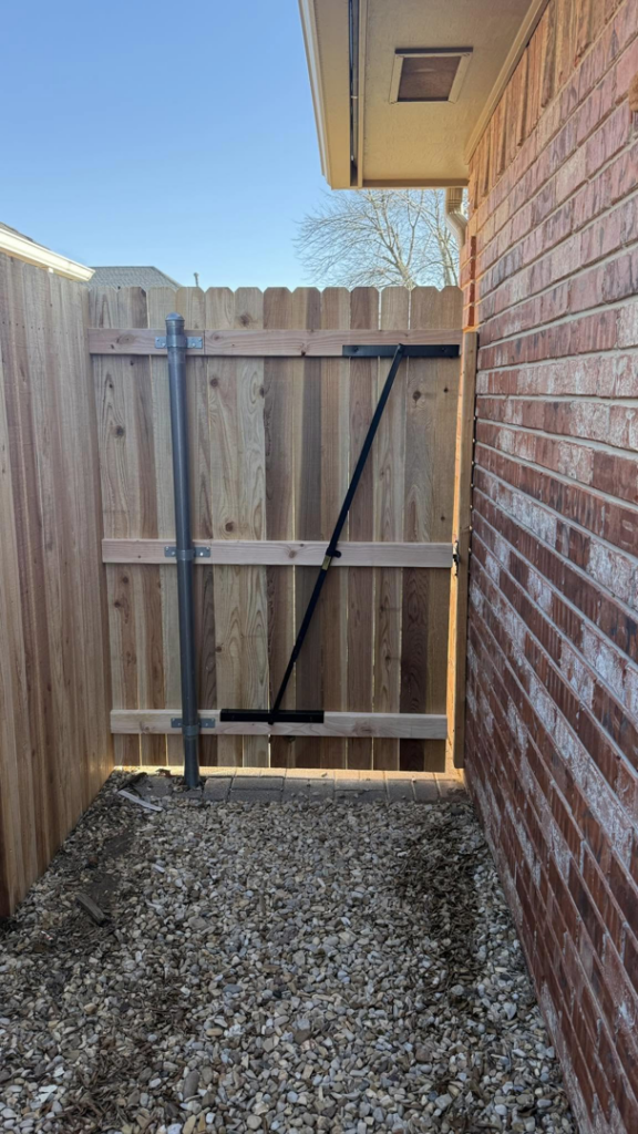 A new wooden gate with metal support and post in a narrow passage by On-Guard Fencing & Gates LLC in Oklahoma City, OK.