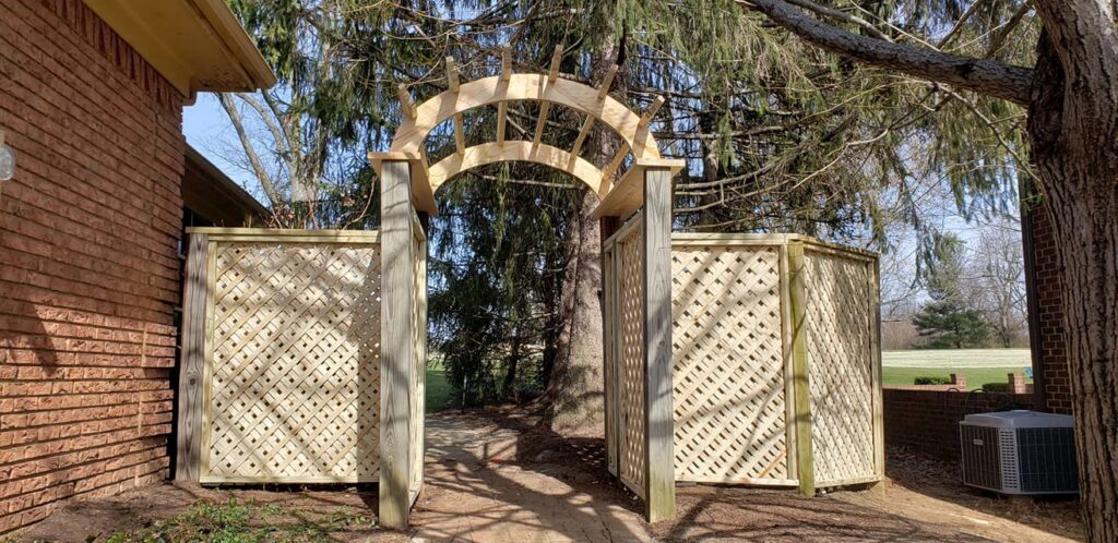 A custom wooden lattice archway and privacy screens installed next to a brick house by Border Built Fencing in Florence, KY.