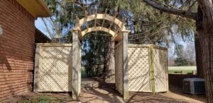 A custom wooden lattice archway and privacy screens installed next to a brick house by Border Built Fencing in Florence, KY.