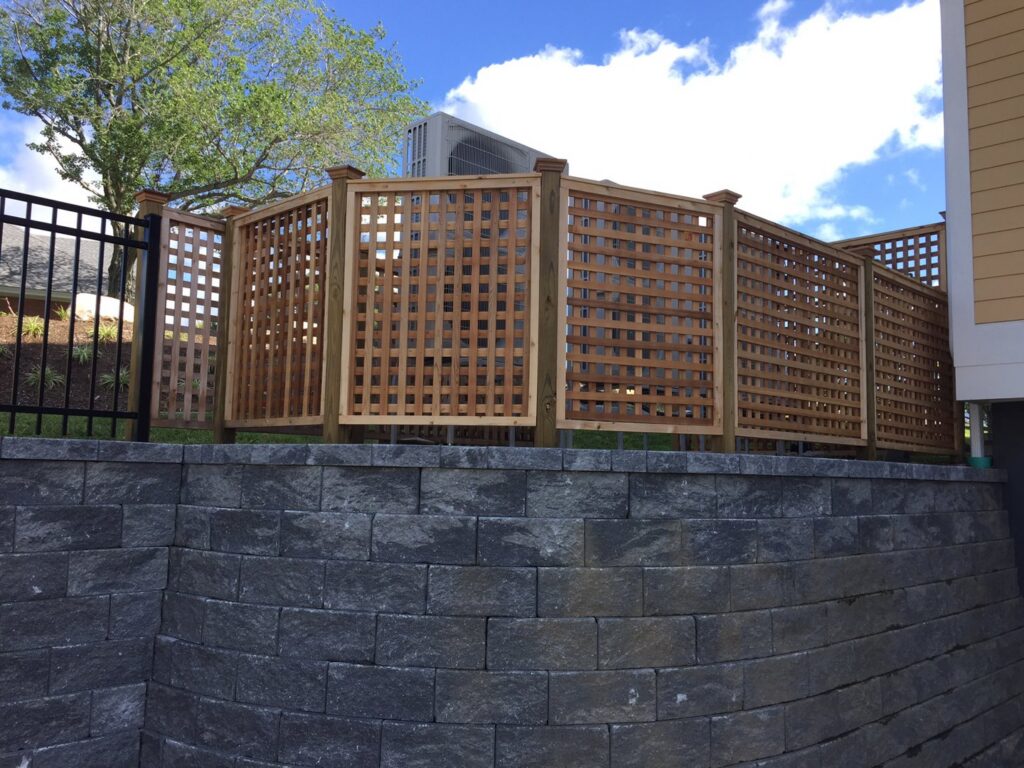 A decorative wooden lattice fence installed on top of a stone retaining wall by Brodeur-Campbell Fence Co. in Springfield, MA.