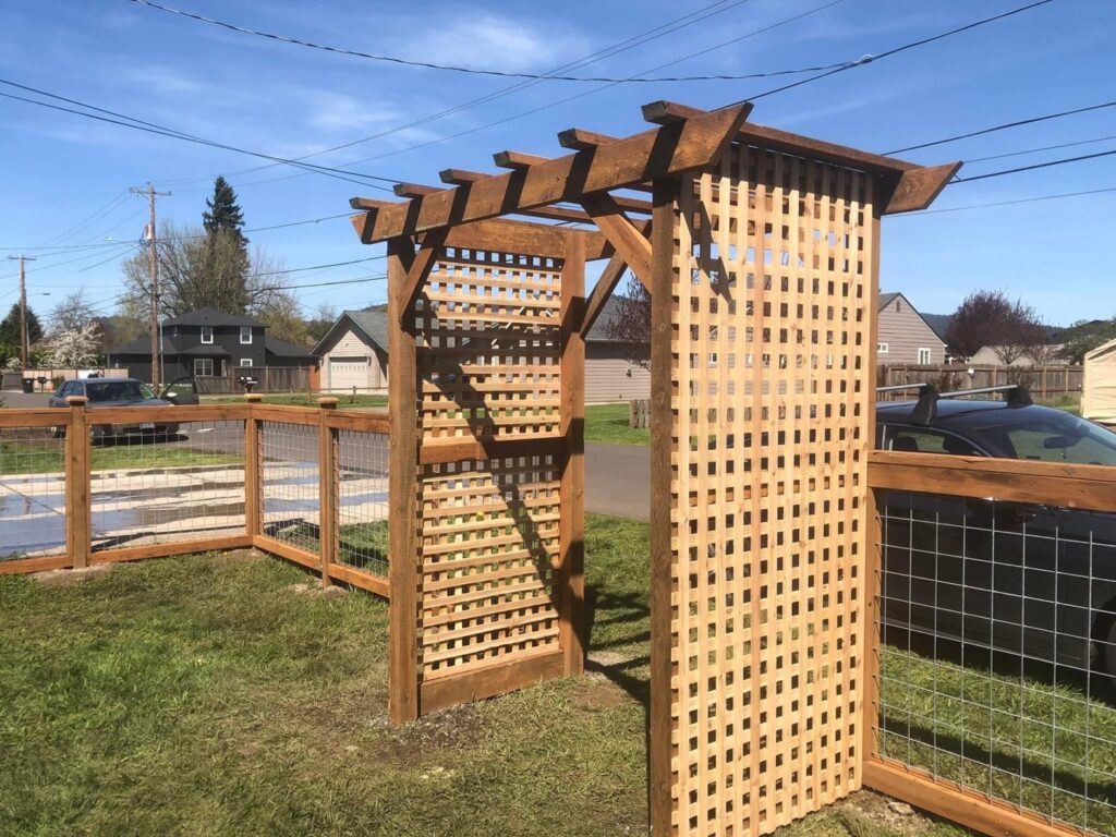 A wooden pergola with lattice work connected to a wire mesh fence by Pacific Woods Fence and Deck in Springfield, OR.