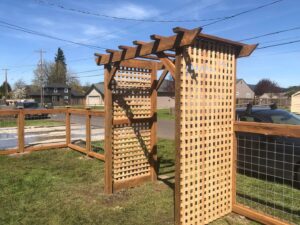 A wooden pergola with lattice work connected to a wire mesh fence by Pacific Woods Fence and Deck in Springfield, OR.