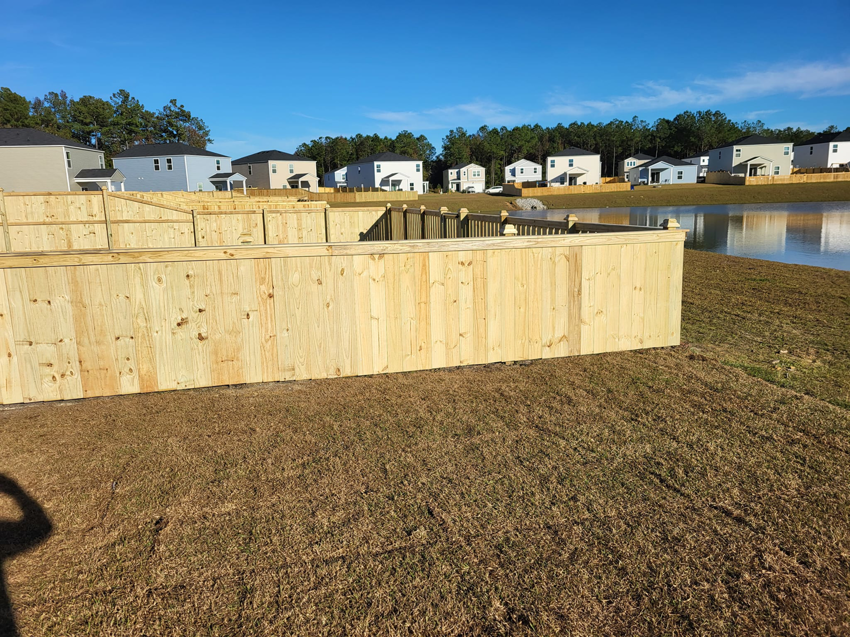 A newly installed wooden picket fence running along a pond in a residential area by Lundquist Home Improvements in Mount Pleasant, SC.