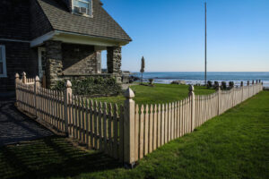 A wooden picket fence installed along a coastal property by Fence Pros Direct in Saunderstown, RI.