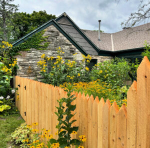A charming wooden picket fence with pointed tops surrounding a vibrant garden by Chisel + Vine in Milwaukee, WI.