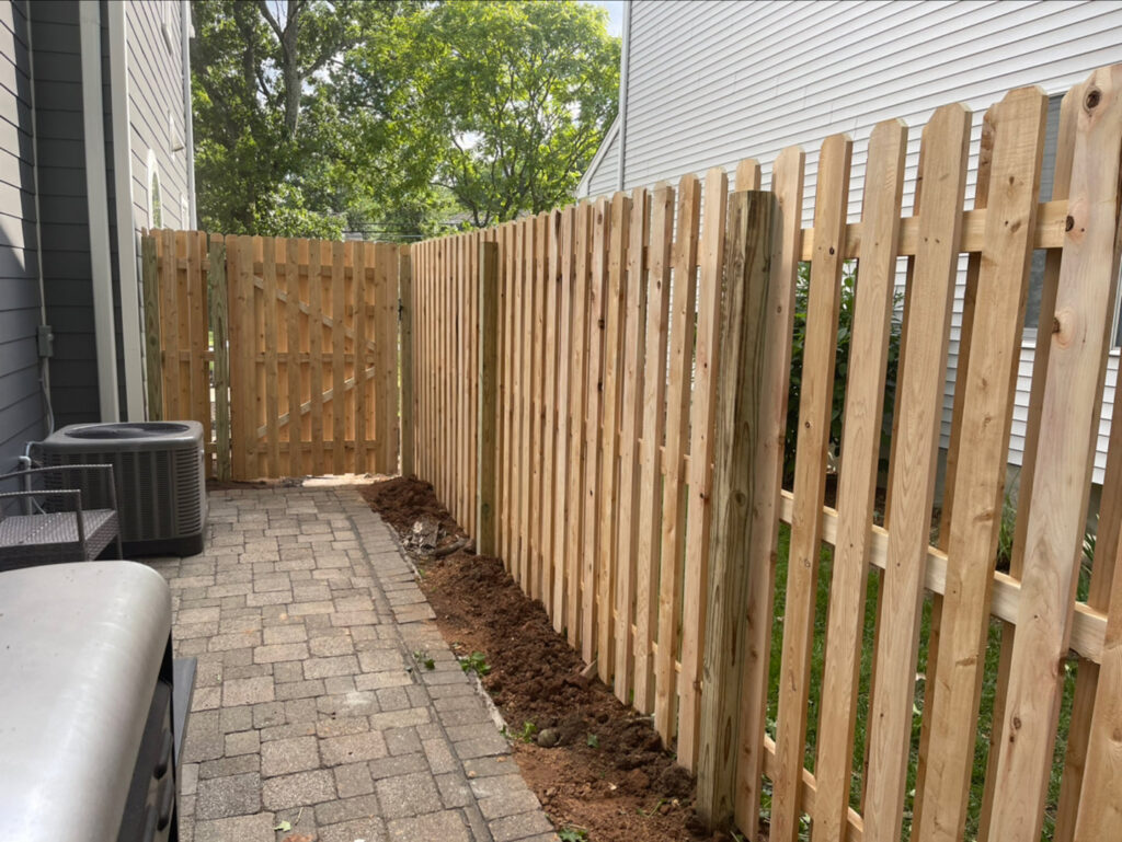 A newly installed wooden picket fence with a gate next to a house by Brothers Fence in Elizabeth, NJ.